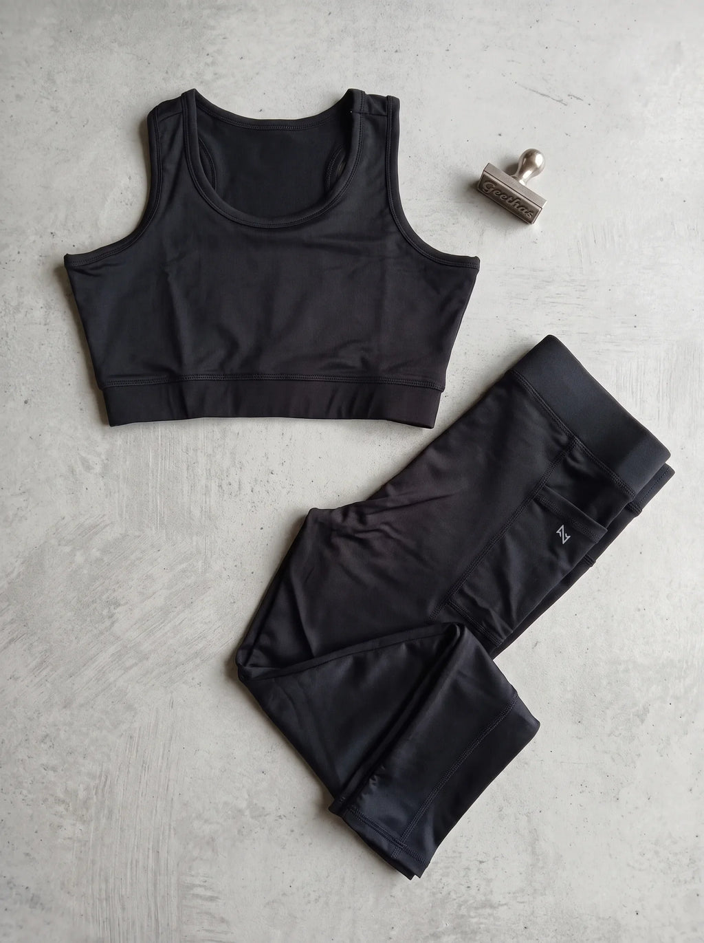 Black sleeveless gym crop top and matching pocket-detail leggings displayed flat