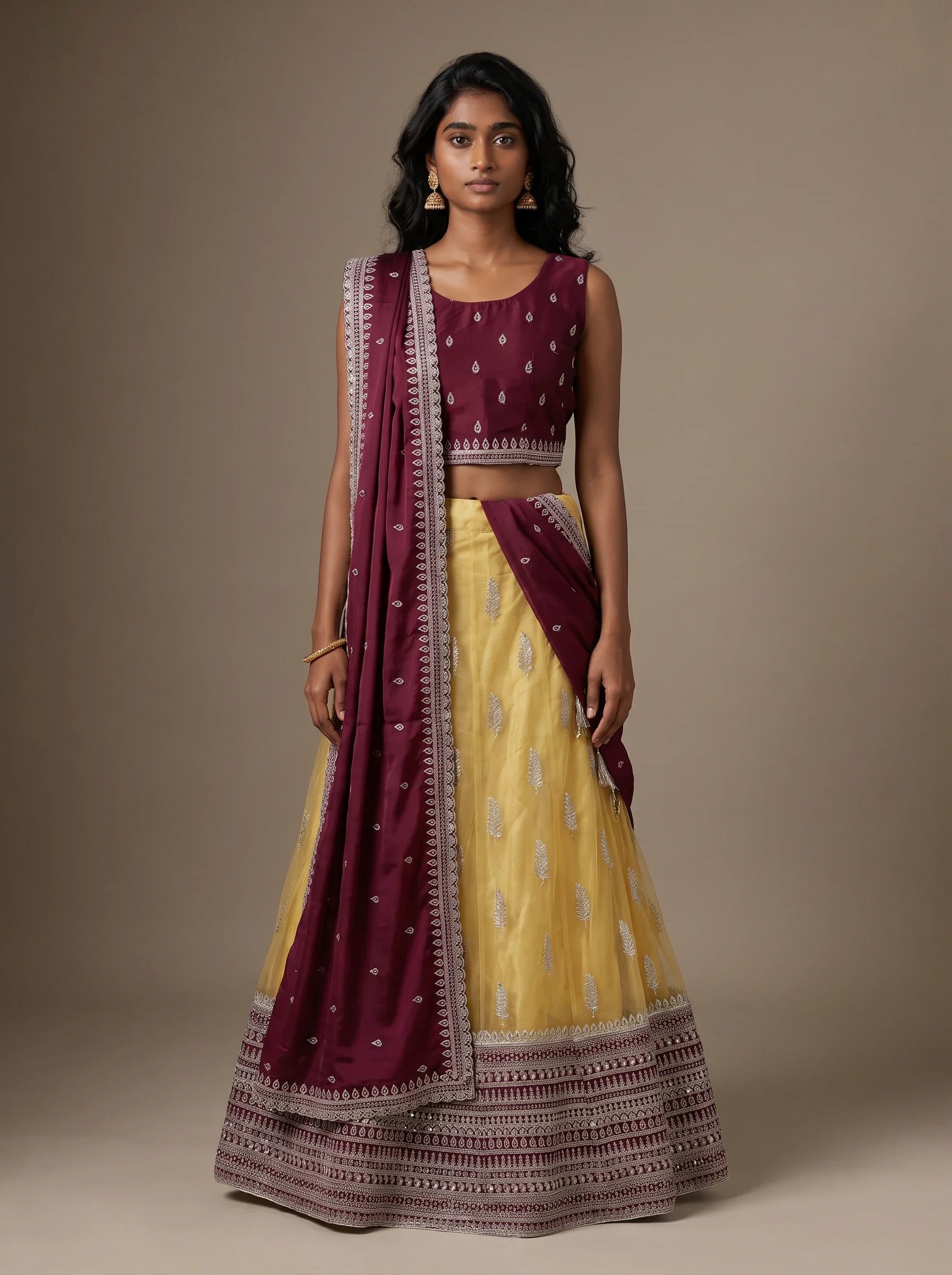 Model wearing a wine and mustard yellow embroidered lehenga set with matching wine dupatta