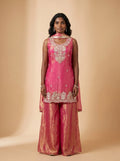 Model wearing a fuchsia pink and metallic gold tissue silk sharara set with embellished top and matching dupatta