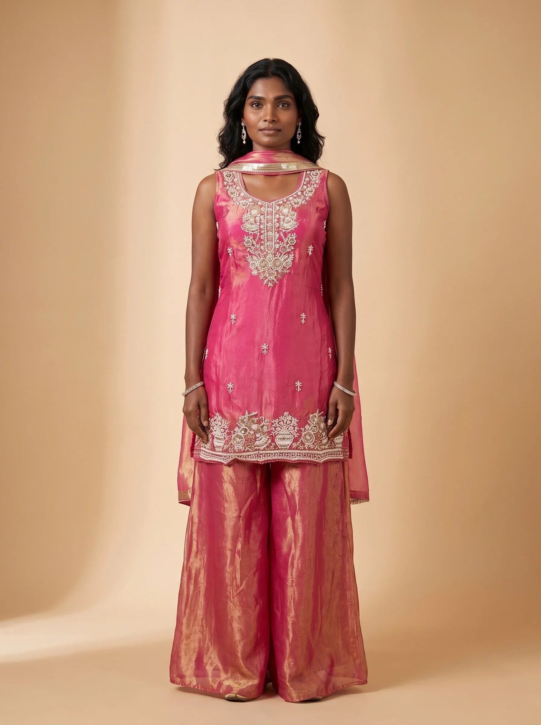 Model wearing a fuchsia pink and metallic gold tissue silk sharara set with embellished top and matching dupatta