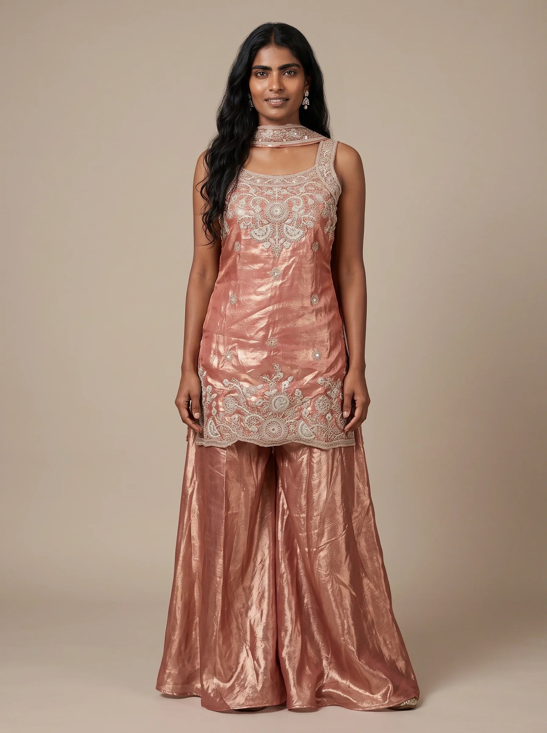Model wearing a peach tissue silk embroidered sharara set with flared bottoms and matching dupatta.