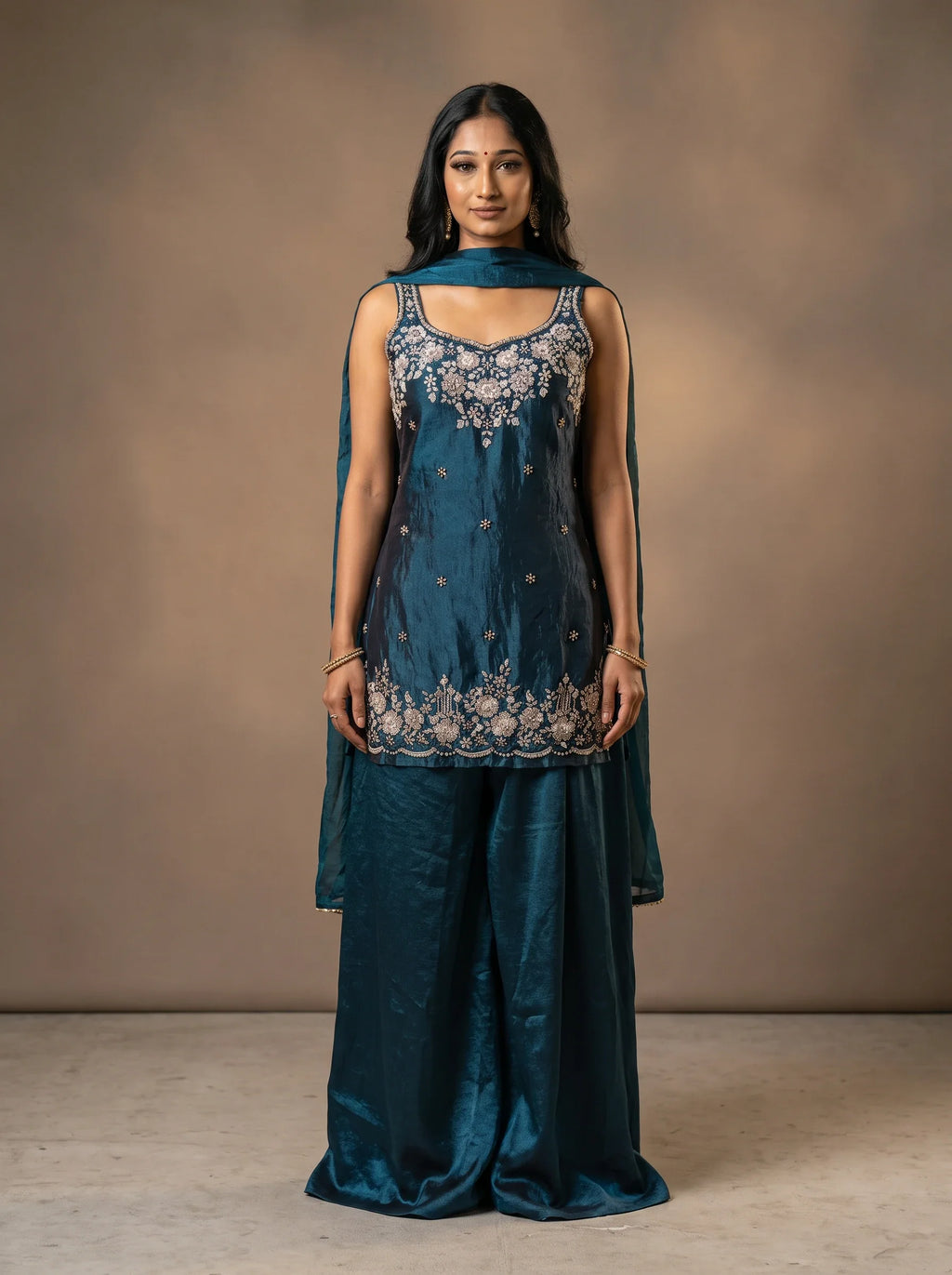 Model wearing a deep teal blue tissue silk sharara set with floral sequin and cut-bead embellished top and matching dupatta.