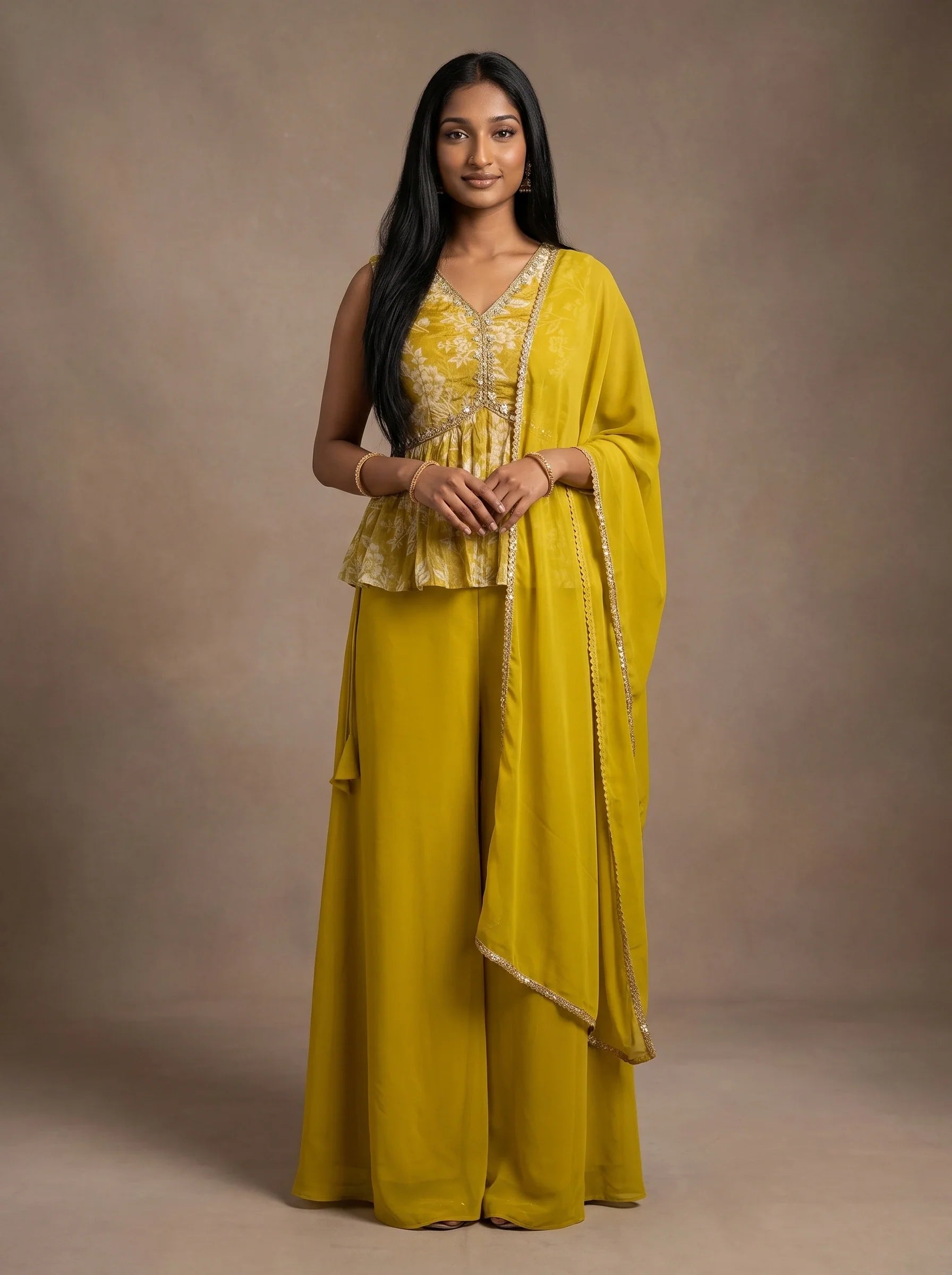 Model wearing a mustard yellow georgette floral peplum sharara set with matching embellished-border dupatta