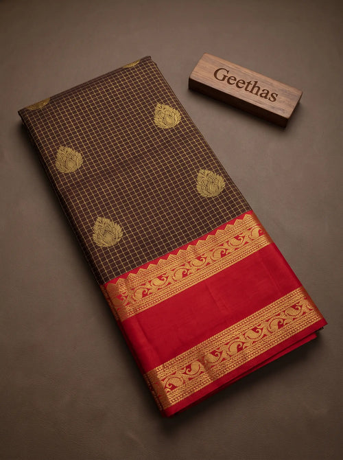 Folded brown soft silk saree showing gold-toned floral motifs, grid pattern and deep red woven border