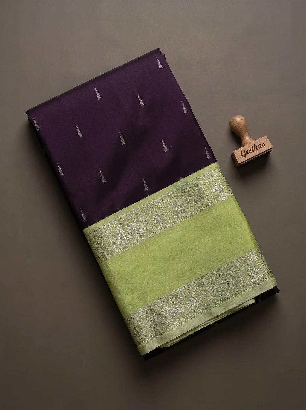 Folded dark wine soft silk saree showing woven motifs and light green geometric border