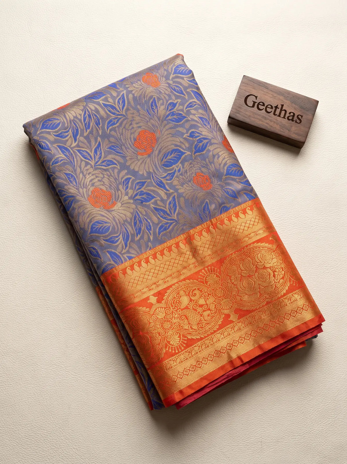 Folded royal blue soft silk saree showing floral woven motifs and a contrasting red-orange gold-toned border